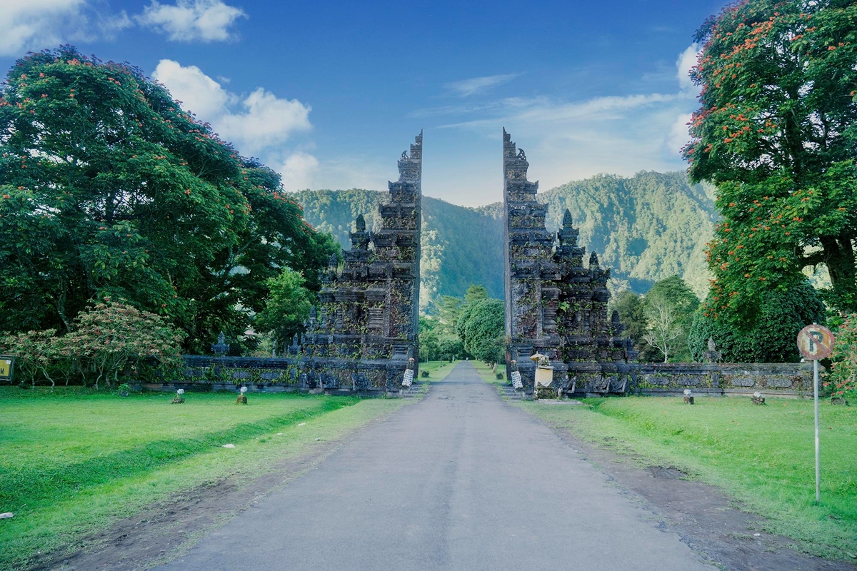 Traditional Balinese candi bentar split gate on a road with mountains behind, Bali